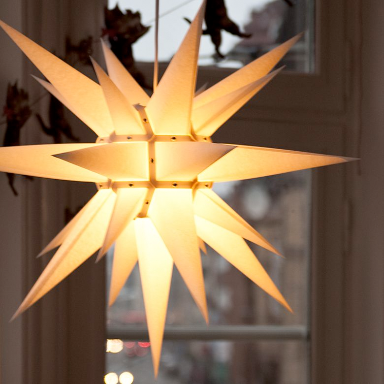 Herrnhuterstjerne i hvid papir som julebelysning, hængende i vindue og skabende varm julestemning.