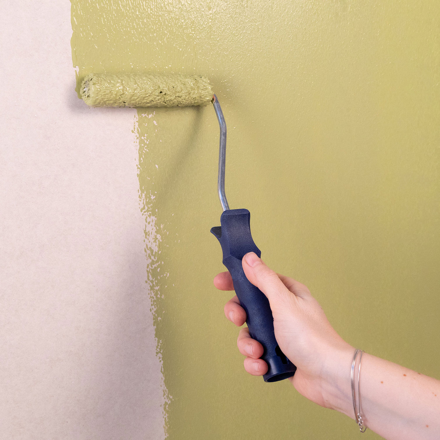 Hånd, der ruller lysegrøn maling på vægg.