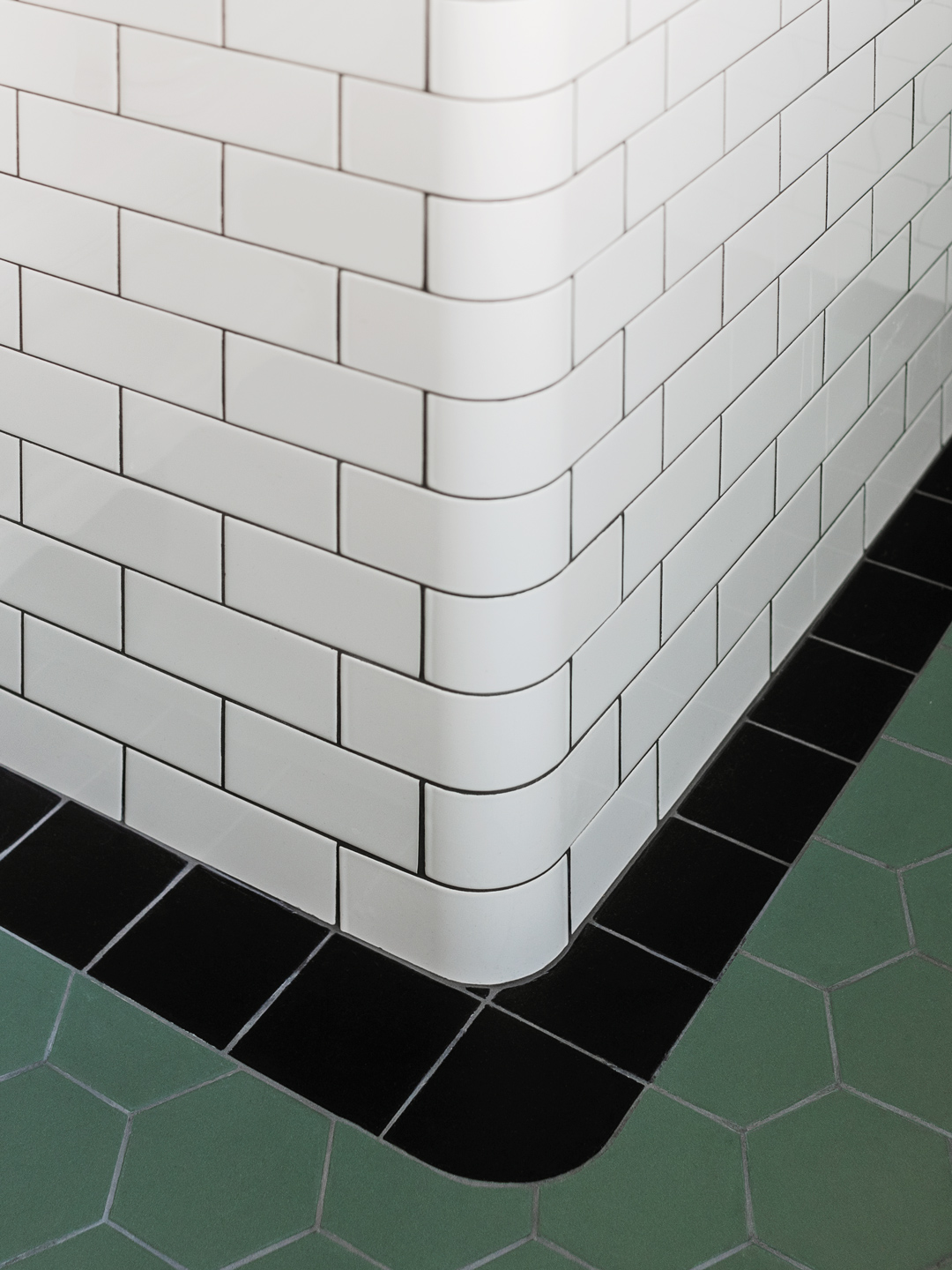 Detalje af hj&oslash;rne med hvide fliser, sort klinkerkant og gr&oslash;nne gulvklinker