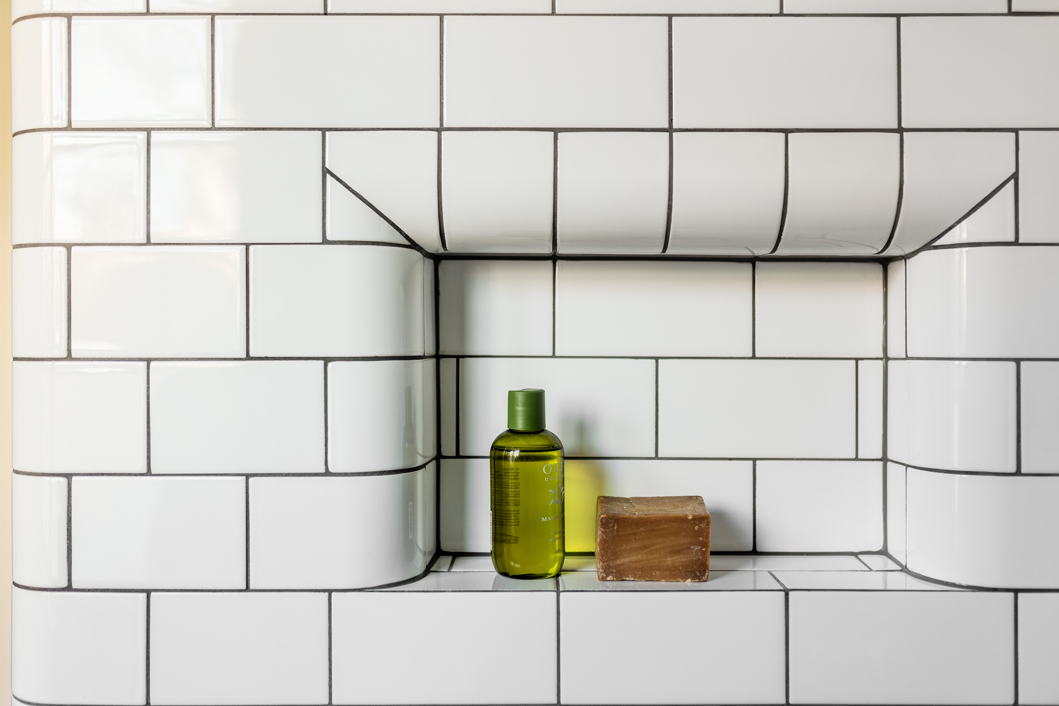 Indbygget niche med hvide fliser, gr&oslash;n flaske og brun s&aelig;be