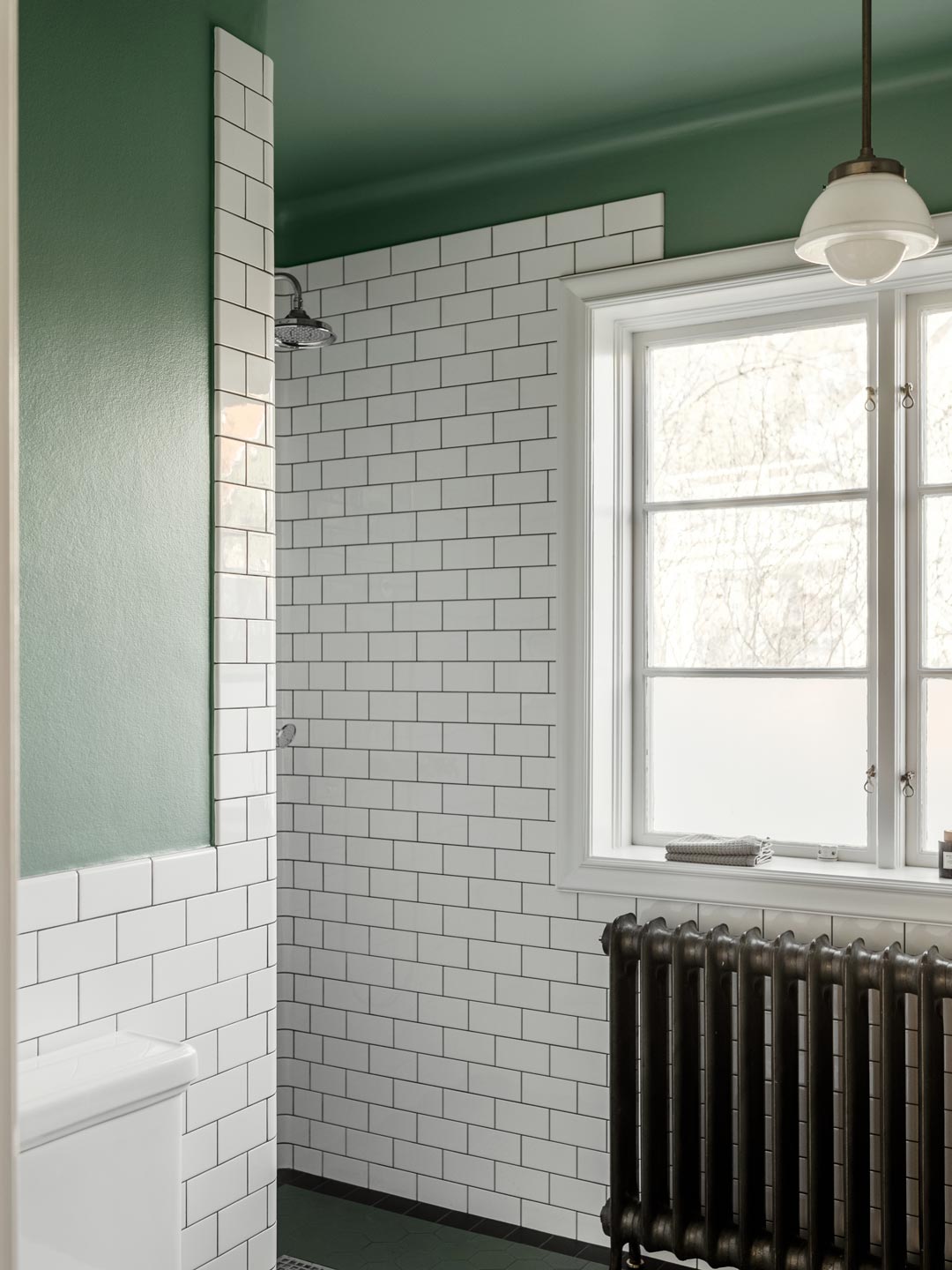 Badev&aelig;relse med gr&oslash;nne v&aelig;gge, hvide metrofliser, sort radiator og bruser