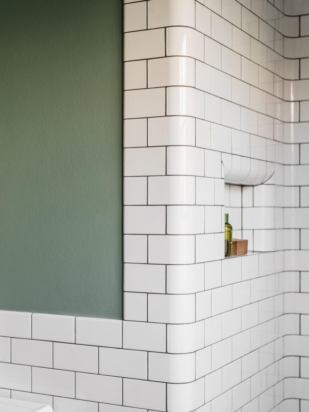 Detalje af badev&aelig;relse med gr&oslash;n v&aelig;g, hvide fliser og indbygget niche