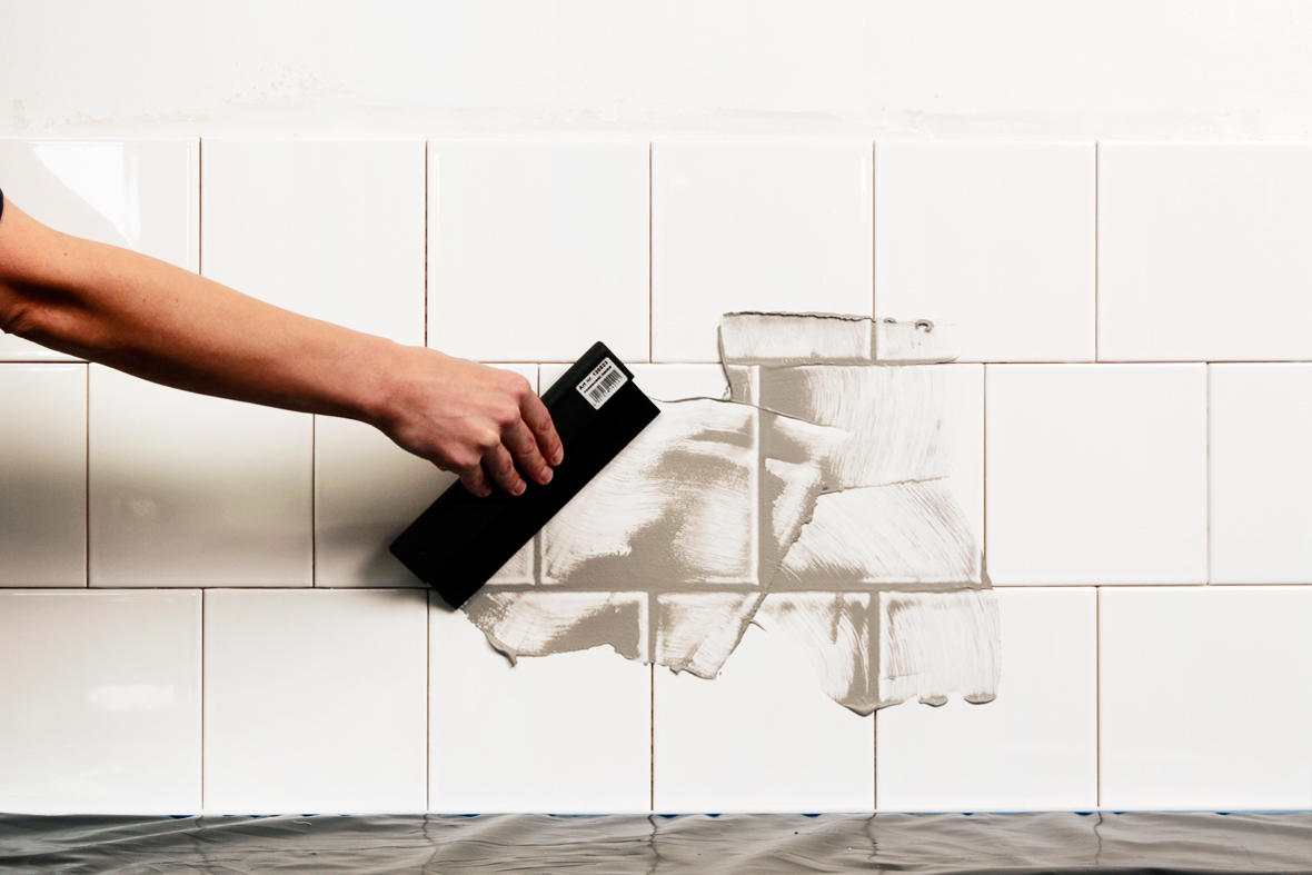 Fordeling af fugemasse med gummispartel over fliserne.