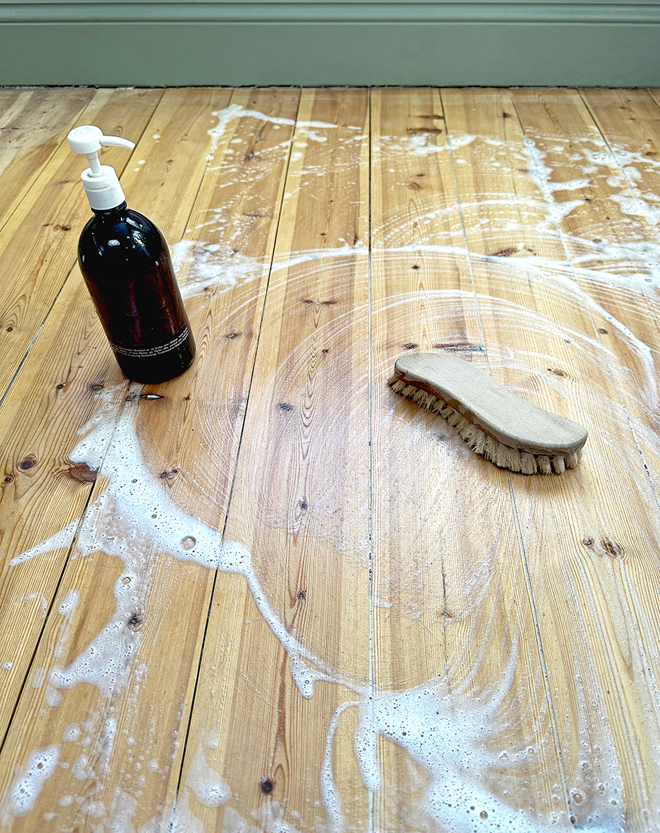 S&aring;pa och skurborste p&aring; ett s&aring;pat br&auml;dgolv.