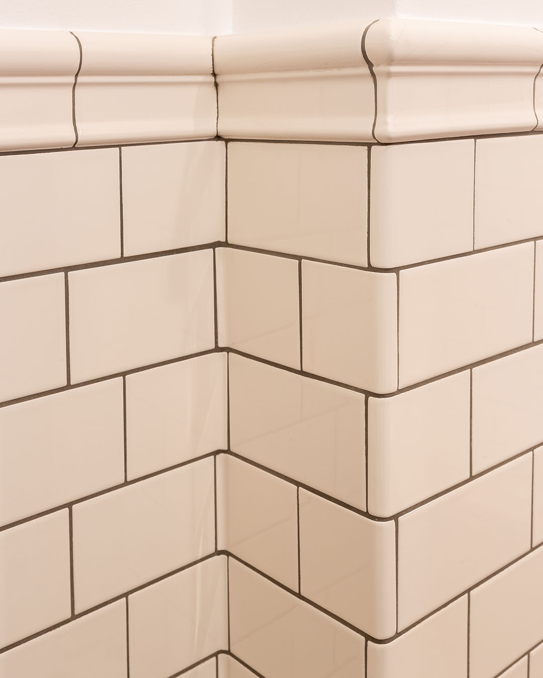 Hvide blanke fliser med m&oslash;rke fuger og afslutningsliste i hj&oslash;rne af badev&aelig;relse.