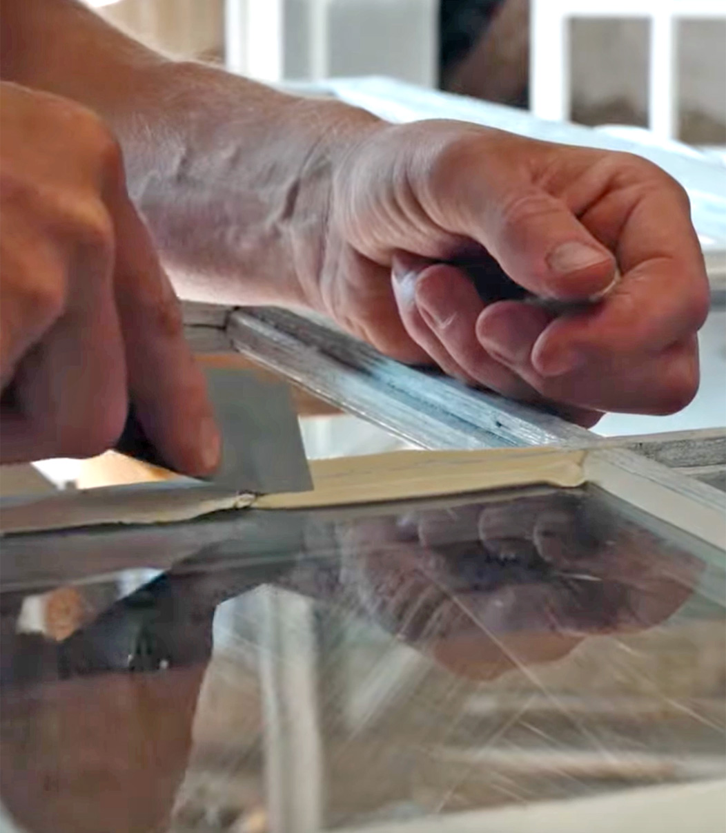 To h&aelig;nder p&aring; billedet l&aelig;gger nyt kit p&aring; et sprossevindue.