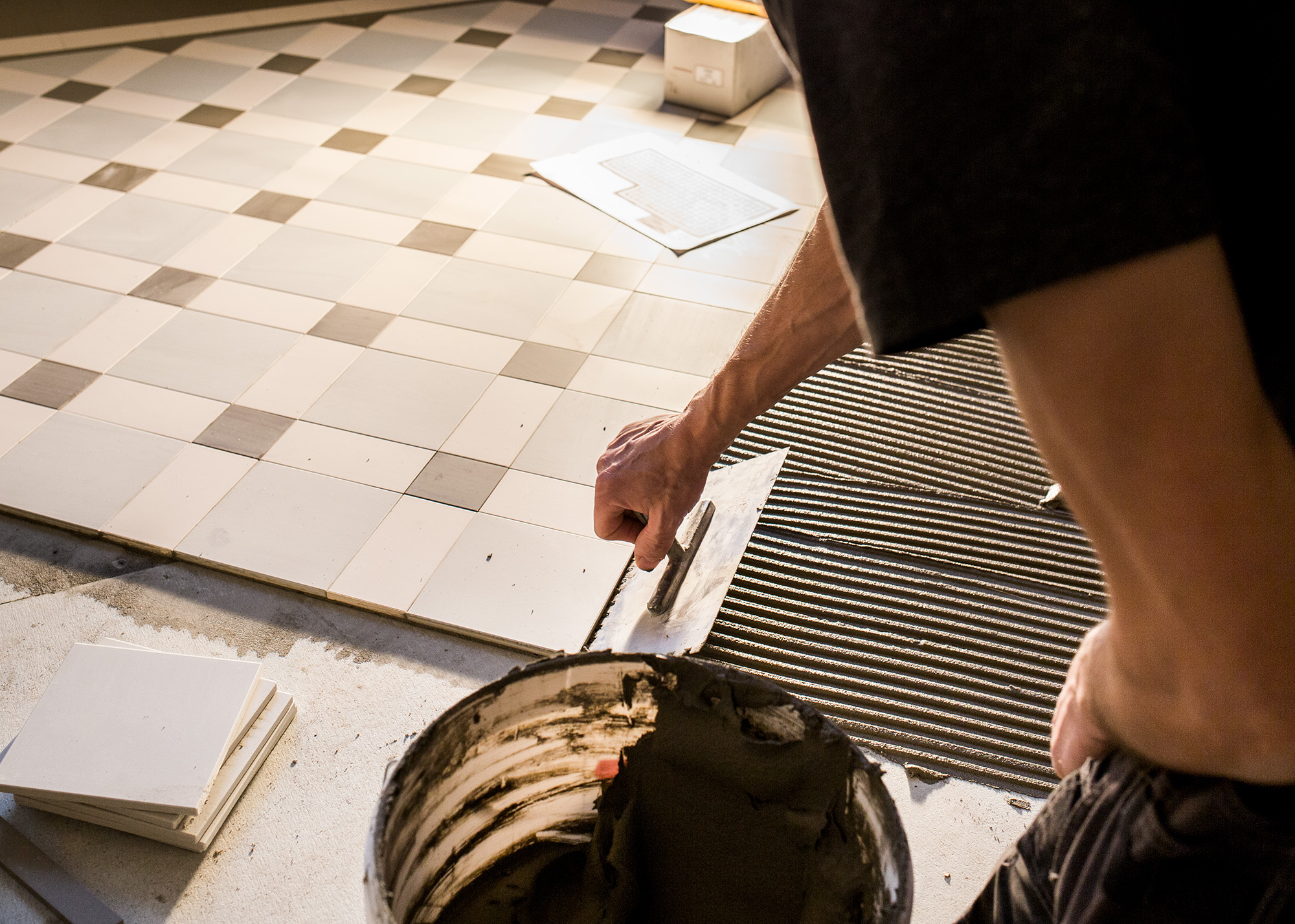 L&aelig;gning af klassiske gulvfliser i m&oslash;nster, flisekl&aelig;b fordeles med tandspartel.