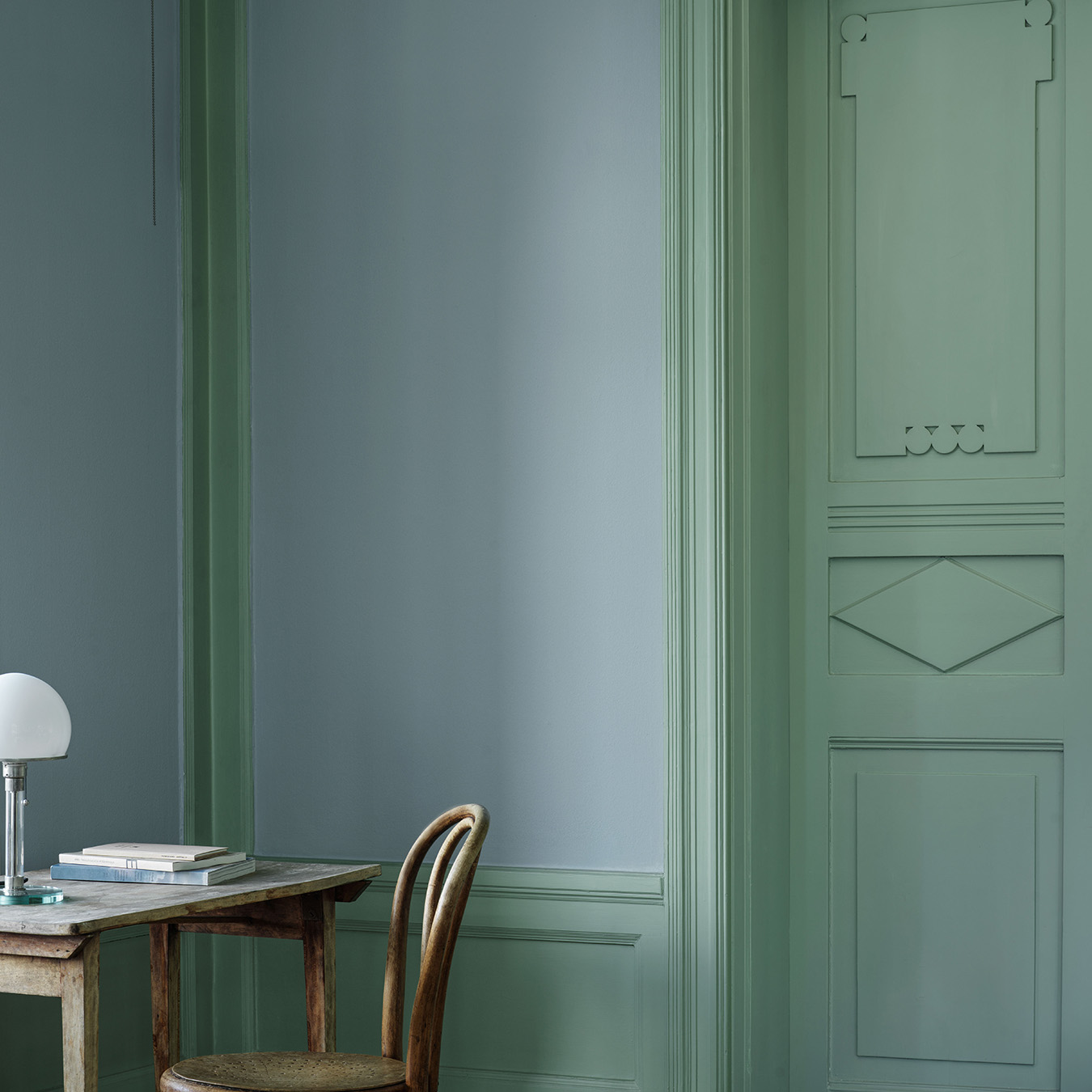 V&aelig;g i farven Mildbl&aring; og fyldningsd&oslash;r samt paneler i farven Tall, med skrivebord og stol i rummet.