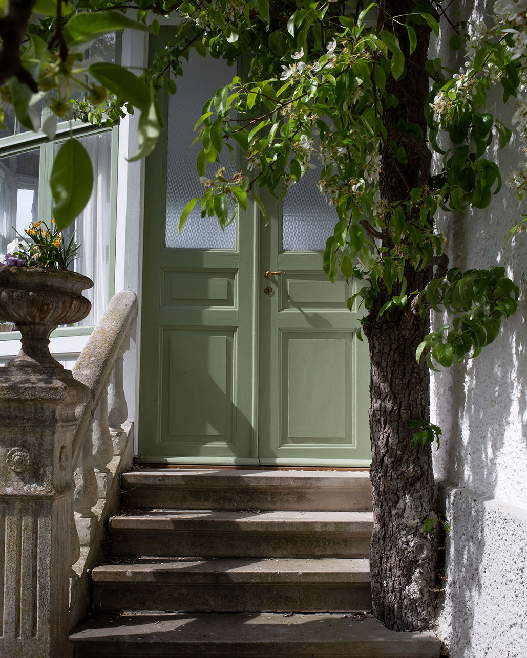 Ytterd&ouml;rr ovanf&ouml;r stentrappa med pelare till vitputsat hus. D&ouml;rren &auml;r m&aring;lad med degebergagr&ouml;n linoljef&auml;rg.