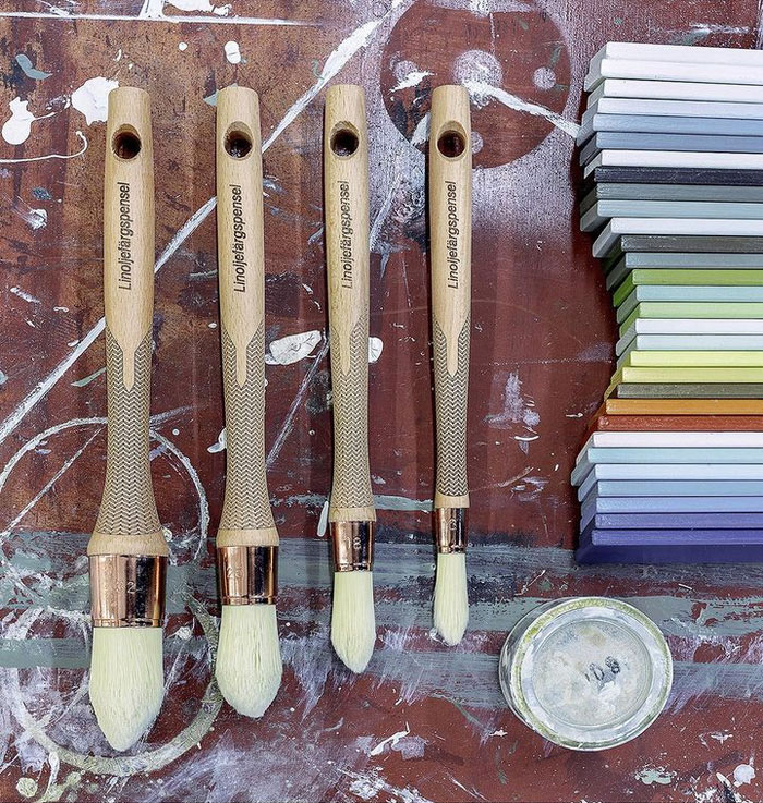 Linoliemalingspensler og pr&oslash;vestykker p&aring; en arbejdsb&aelig;nk med malingspletter.
