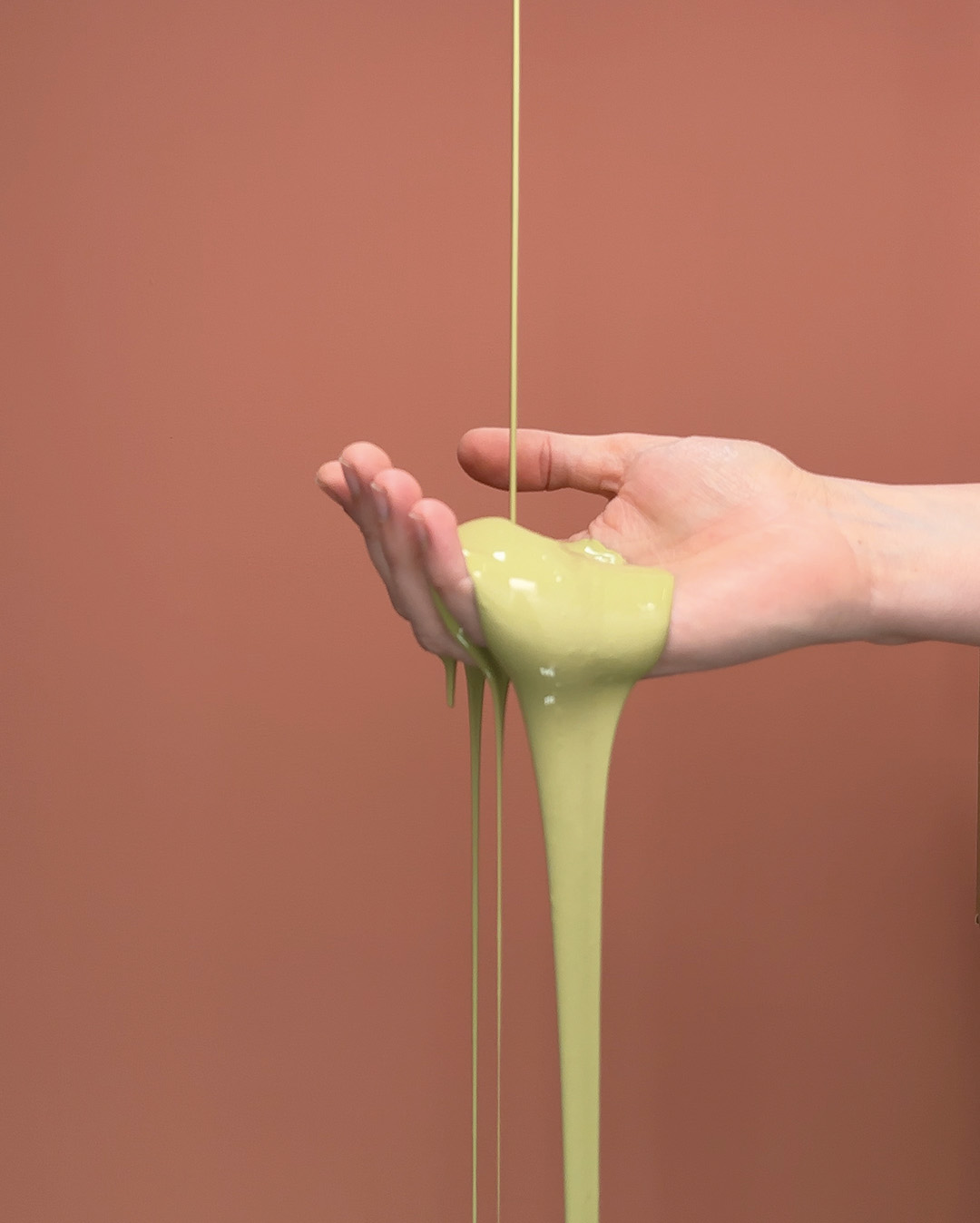 H&aring;nd med gr&oslash;n maling, der h&aelig;ldes ud mod baggrund i r&oslash;d.