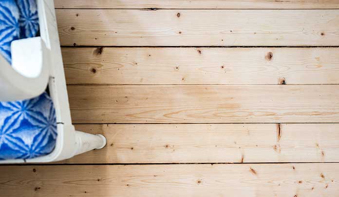 S&aring;paskurat br&auml;dgolv med vit k&ouml;kssoffa med bl&aring; dyna.