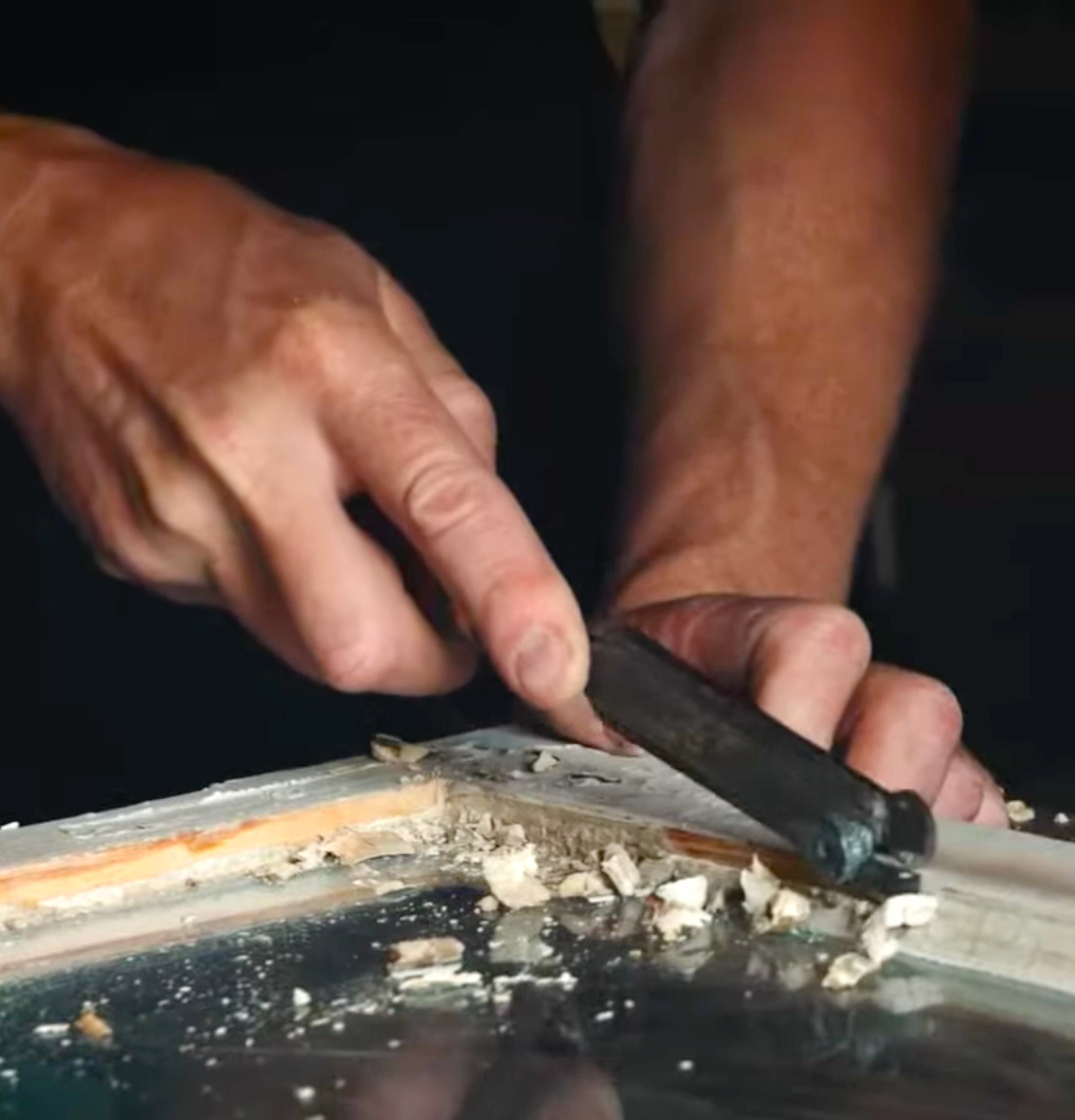 To h&aelig;nder, der skraber en vinduesramme fri for gammelt kit.