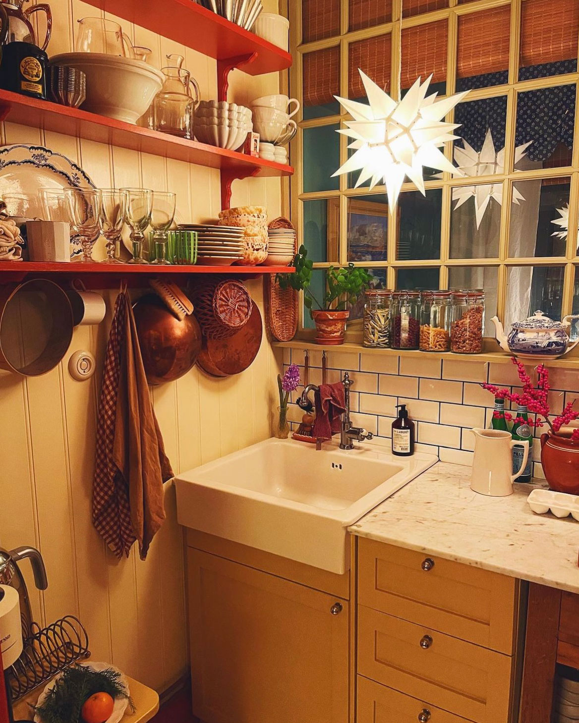 Herrnhuterstjerne som julelampe over k&oslash;kkenbord med gule skabe, hylder med service og julestemning.