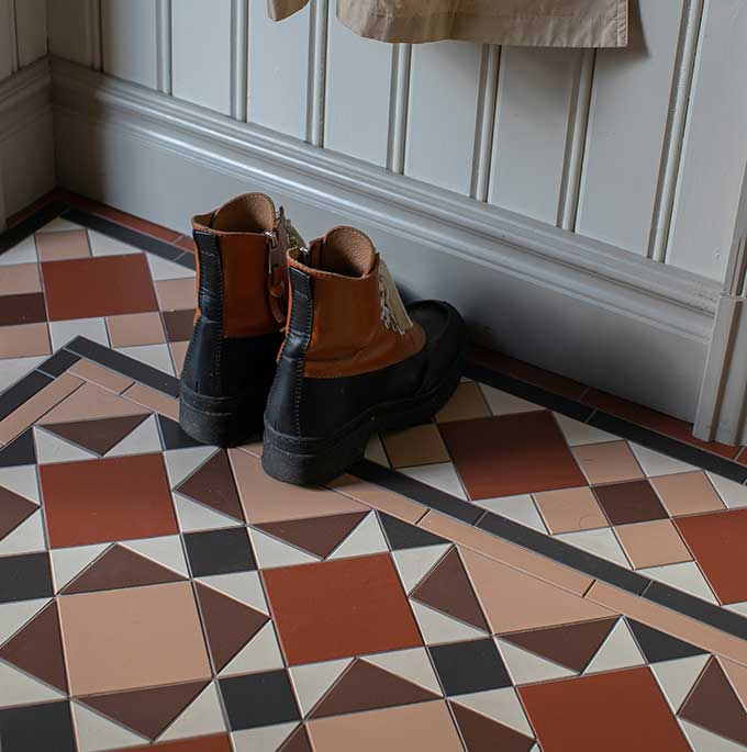 M&ouml;nstrat klinkergolv med flera olika former i bruna, r&ouml;da och vita toner mot p&auml;rlspontspanel i gr&aring;tt.